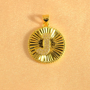 Macro shot of gold sunburst pendant with letter J and micro-paved sparkling crystals