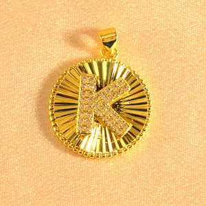Macro shot of gold plated sunburst pendant featuring letter K set with sparkling zircons