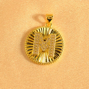 Macro shot of gold-plated sunburst pendant featuring an iced-out crystal letter M detail
