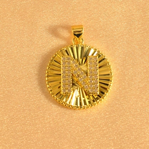 Macro detail of gold-plated sunburst pendant featuring crystal-encrusted letter N