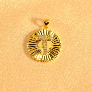 Detail showing gold-plated circular pendant with sunburst texture and pavé zircon letter T