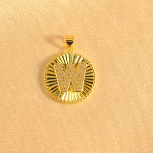Detail of gold circular pendant with micro-paved cubic zirconia letter W and sunburst texture
