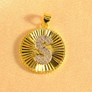 Macro detail of gold-plated sunburst pendant featuring micro-pave cubic zirconia letter S