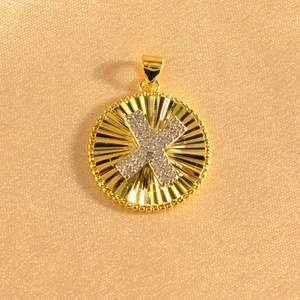 Detail of gold sunburst pendant with crystal-encrusted letter X on shimmering fabric