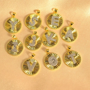Gold plated round pendants with sunburst pattern and iced-out alphabet letter charms.