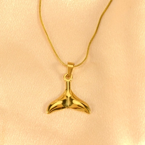 Detail eines polierten goldenen Fischschwanz-Anhängers an einer feinen Schlangenkette