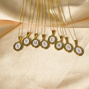 Golden oval alphabet necklaces with white enamel drip on luxury champagne satin background