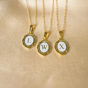 Detailed macro view of gold-plated oval alphabet pendants L, W, X with white enamel inlay