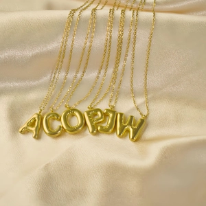 Detail von 3D-Bubble-Buchstabenanhängern in Gold auf luxuriöser Champagner-Seide