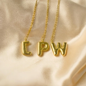 Makroaufnahme von Gold-Buchstabenanhängern L P W auf glattem Seidenstoffhintergrund