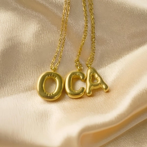 Nahaufnahme der goldenen Buchstaben O C A Anhänger auf seidigem Champagner-Satin