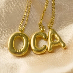 Minimalistische goldene Buchstaben-Halsketten A, C und O auf Satinhintergrund