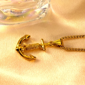 Gold stainless steel anchor pendant necklace with rope detail on a silk background