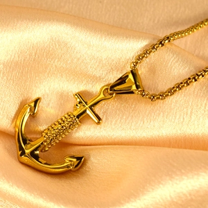 Gold anchor pendant necklace with cross detail and box chain on luxury satin background