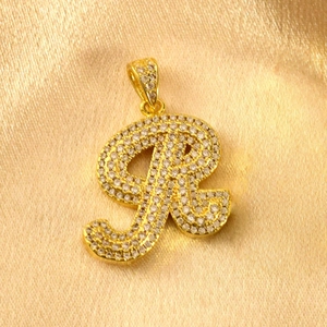 Detailaufnahme eines goldenen Zirkonia-Buchstaben-R-Anhängers auf glänzendem Seidenstoff.