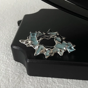 Detailed view of silver lava metal brooch with light blue enamel and square crystals