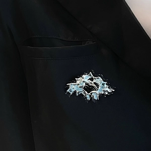 Detail of silver liquid metal brooch with light blue crystals on black suit blazer