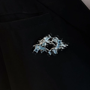 Artistic silver pleated metal brooch with light blue crystals on black blazer lapel