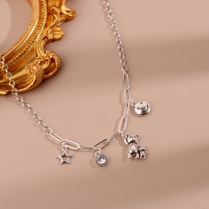 Détail des pendentifs ours et étoile sur une chaîne de pull argentée à maillons