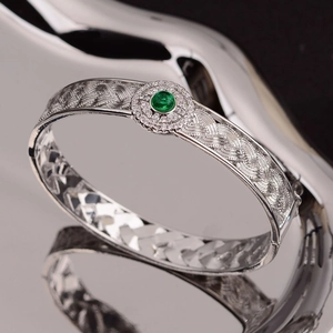 Silver woven open bangle featuring a round green gemstone surrounded by sparkling crystals