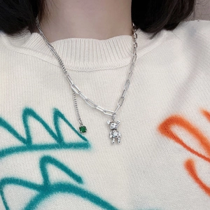 Détail du collier ours avec pierre émeraude sur un pull en maille blanche