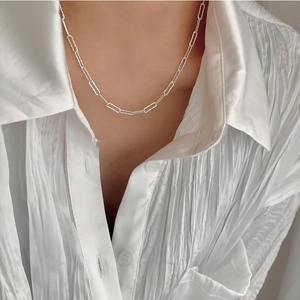 Macro detail of silver paperclip chain necklace with textured finish on white shirt
