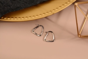 Dettaglio di orecchini geometrici argentati con finitura a specchio su sfondo rosa