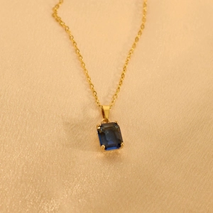 Detail eines blauen Edelsteinanhängers an einer Goldkette auf seidigem Hintergrundgewebe