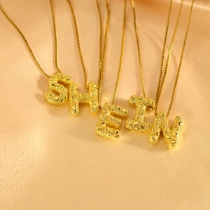 Goldene Buchstaben-Halsketten mit Hammerschlag-Struktur auf Champagner-Seidenhintergrund
