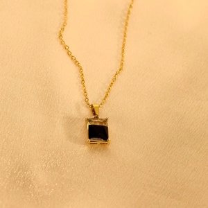 Detailansicht eines rechteckigen schwarzen Edelsteinanhängers an einer Goldkette auf Seide