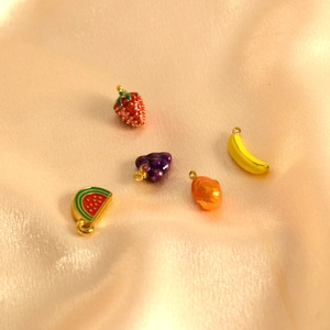 Primer plano de dijes de frutas coloridas como fresa y uva sobre tela de raso