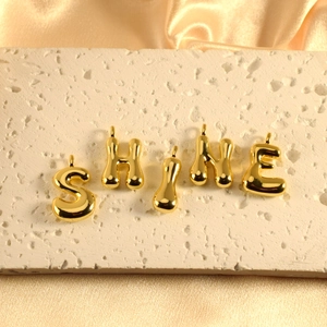 Golden liquid metal bubble alphabet pendant set spelling SHINE on silk background