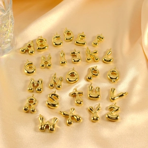 Detailed flat lay of 26 golden balloon-style alphabet pendants on champagne silk fabric