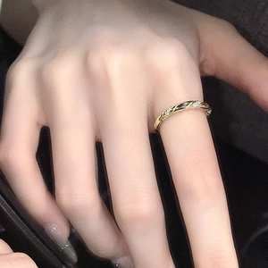 Detail eines dünnen goldenen Wellenrings mit Kristallen, am Finger vor dunklem Hintergrund