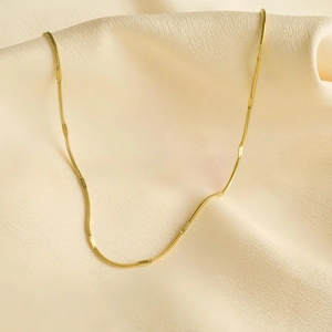 Gros plan d'un collier chaîne serpent dorée sur un fond de soie beige doux