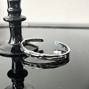 Gothic style silver open cuff bracelet with molten lava texture on black reflective surface