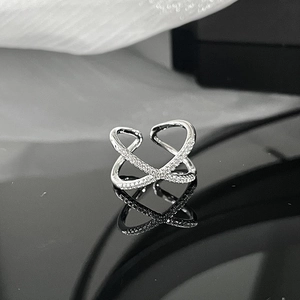 Macro shot of silver crisscross ring with white zircons on black mirror surface