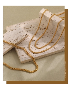 Detail of gold wheat chain necklace with intricate woven texture on travertine stone