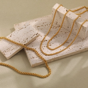 Elegant gold PVD plated wheat chain necklace displayed on a textured stone stand