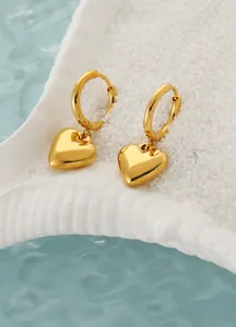 Detailopname van gouden hartvormige oorbellen op witte schelp en blauwe waterachtergrond