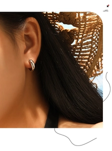 Close-up of polished silver hoop earrings worn by a model against a summer sky background