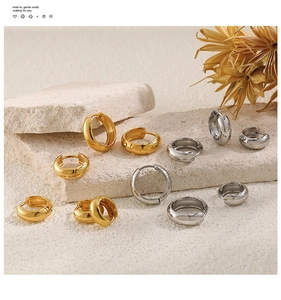 Various sizes of polished gold and silver stainless steel hoop earrings on stone background
