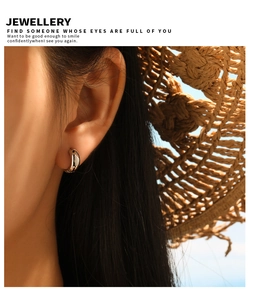 Close-up of golden C-shaped stainless steel hoop earrings worn on ear with summer hat