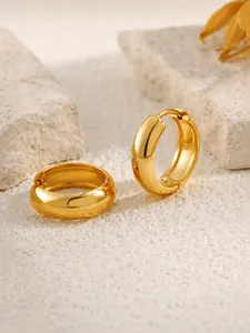 Detailed view of thick gold huggie hoop earrings with polished finish on stone background