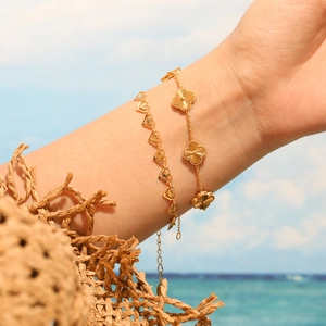 Pulseras de acero dorado con diseño de corazón y trébol lucidas en la muñeca