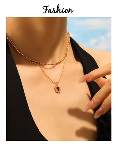 Close-up of double-layer gold necklace with red gemstone heart pendant and bead chain