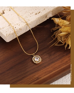Close-up of gold titanium necklace featuring a square zircon pendant on stone background