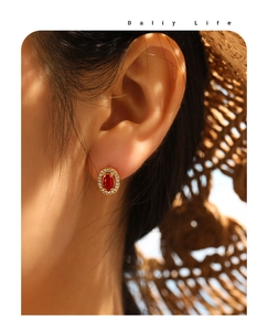 Detail of vintage ruby stud earrings with zircon halo worn by a model in warm light