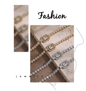 Detail of square-cut crystals and gold-tone tennis chains on a marble surface