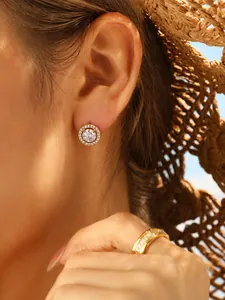 Close-up of sparkling halo stud earrings and a gold band ring worn by a model